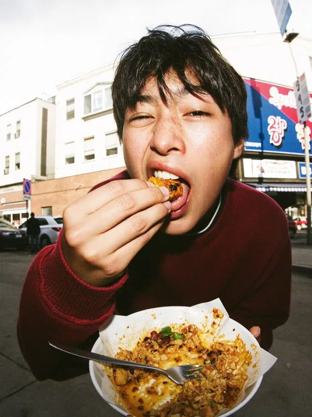 Joven comiendo comida callejera en la calle